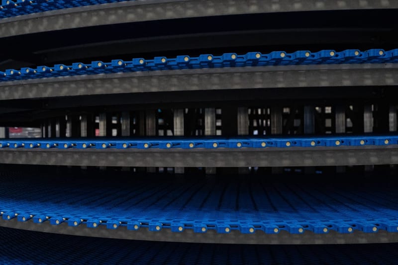 Close view of blue conveyor chain through a cooling assembly