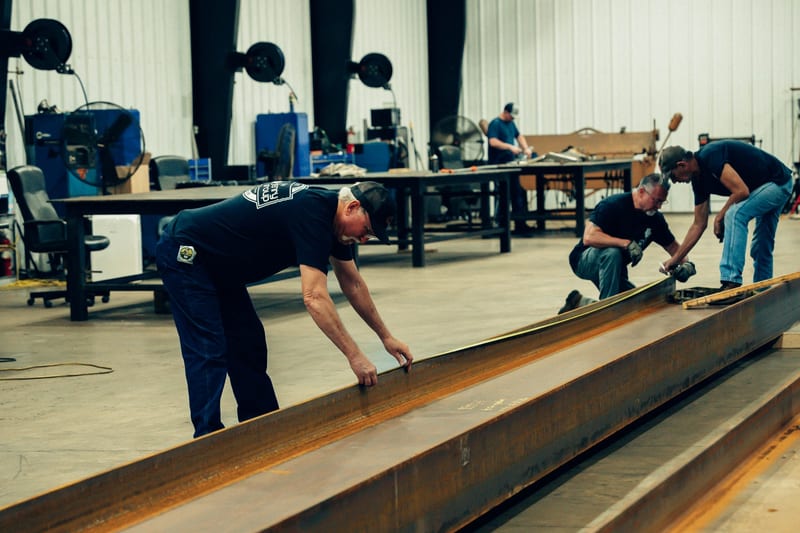 THG fabricators laying out a long steel beam on the shop floor