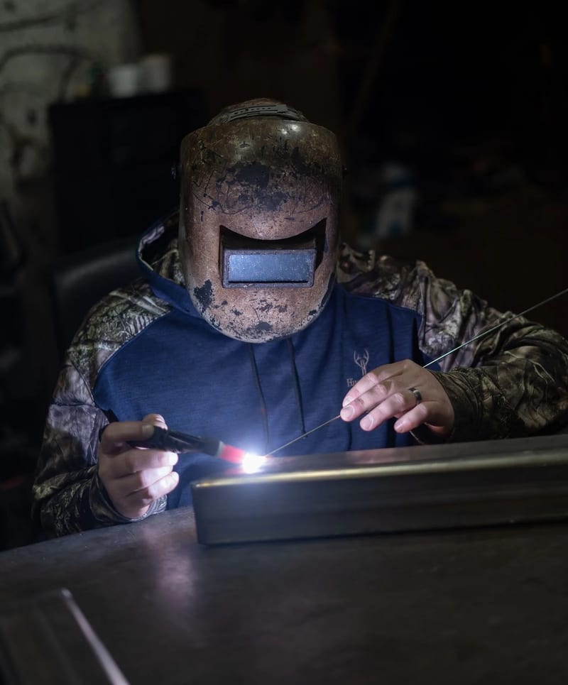 Welder working on a straight metal seam at a shop bench