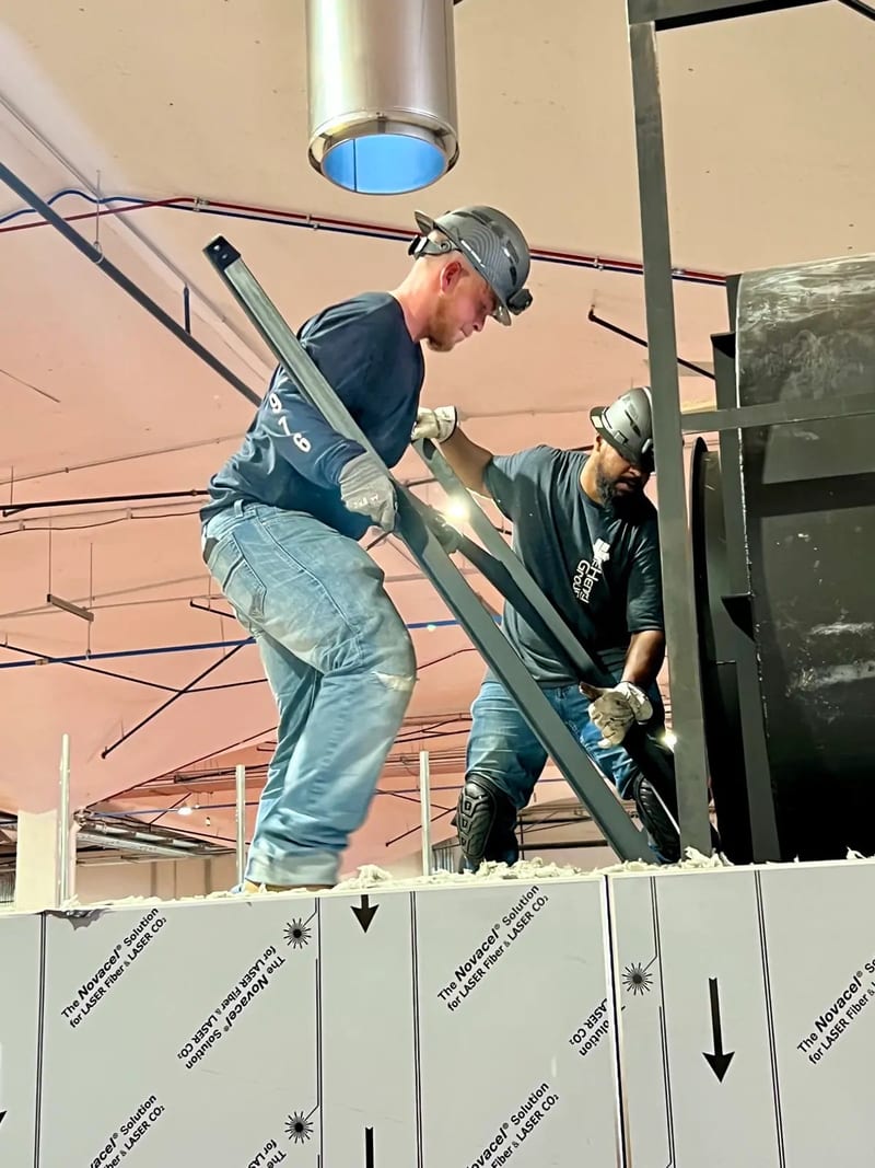 Two Henry Group crew members on top of an oven guiding a steel frame member into place