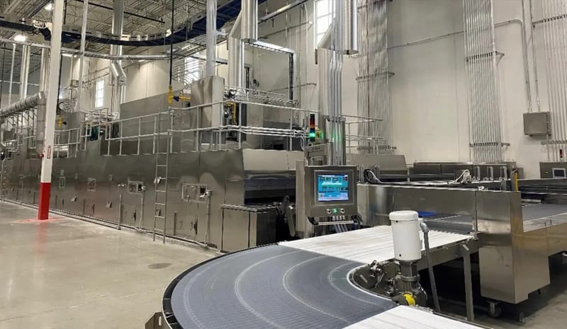 Finished bakery oven line with its HMI control panel and a curving conveyor at the discharge end