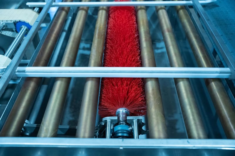 Red brush beneath the rollers of a conveyor assembly