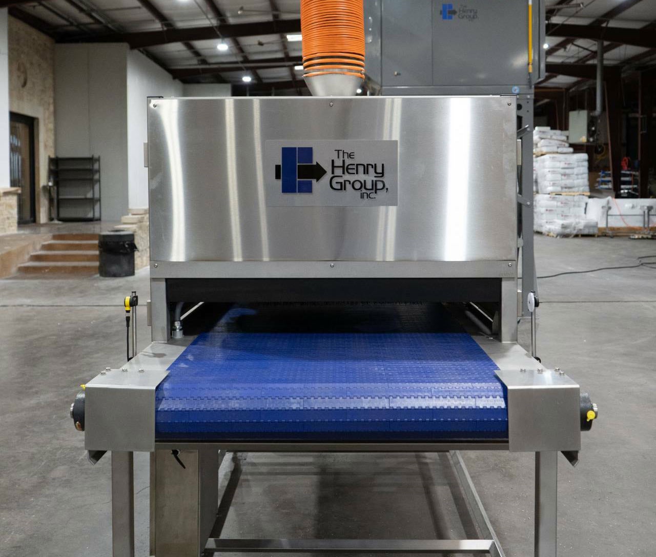 Front view of a THG pan cleaner with its blue infeed belt and extraction duct