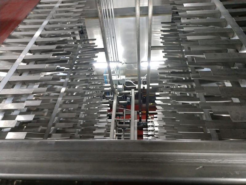 Rows of metal product carriers inside a traveling-tray proofer