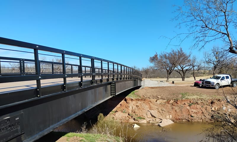 A Roadrunner steel vehicle bridge over a creek, with a pickup at the far end