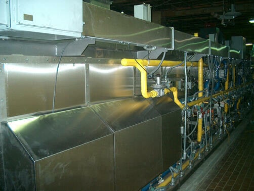 Burner and pipework along a traveling-tray oven